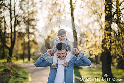 Adorable little daughter sitting on dad`s neck and laughing. Young father walk with his cute daughter in the park Stock Photo