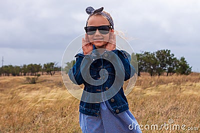 Adorable little girl in a straw hat, blue plaid summer dress in grass field countryside. Child with long blonde braid Stock Photo