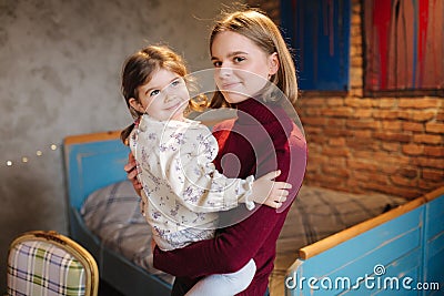 Adorable little girl hug her beautiful and young godmother. Portrait of happy woman hug her goddaughter at home. Cute Stock Photo