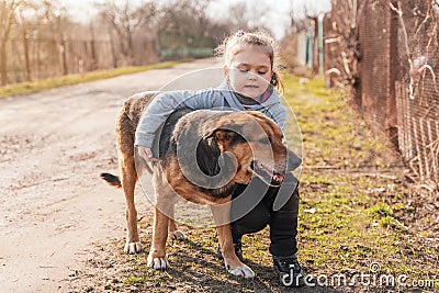 Adorable little girl hugging a large brown yard dog on a village street Stock Photo