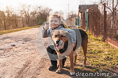 Adorable little girl hugging a large brown yard dog on a village street Stock Photo