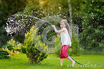 Adorable little girl playing with a garden hose on summer evening Stock Photo