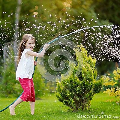 Adorable little girl playing with a garden hose on summer evening Stock Photo