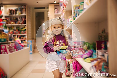 Adorable little girl shopping for toys. Cute female in toy store. Happy young girl selecting toy Stock Photo