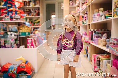 Adorable little girl shopping for toys. Cute female in toy store. Happy young girl selecting toy Stock Photo