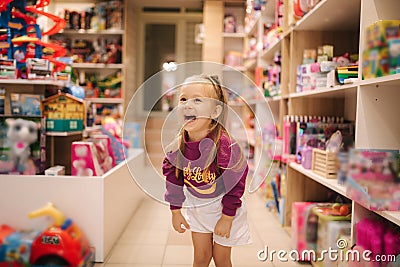 Adorable little girl shopping for toys. Cute female in toy store. Happy young girl selecting toy Stock Photo