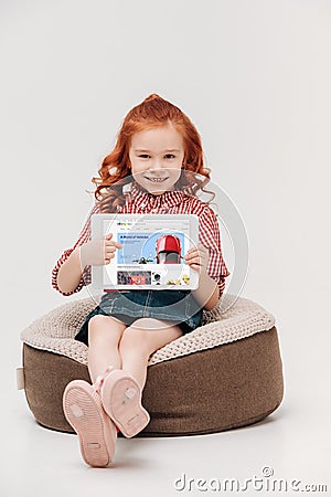 adorable little girl smiling at camera while holding digital tablet with ebay website on screen Editorial Stock Photo