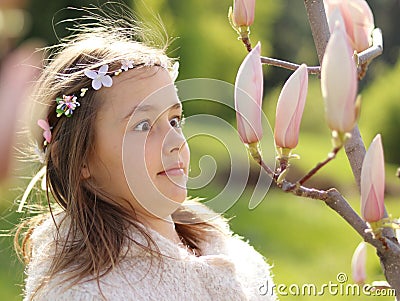 Adorable little girl is surprised and amazed looking at magnolia buds in the blooming spring garden Stock Photo