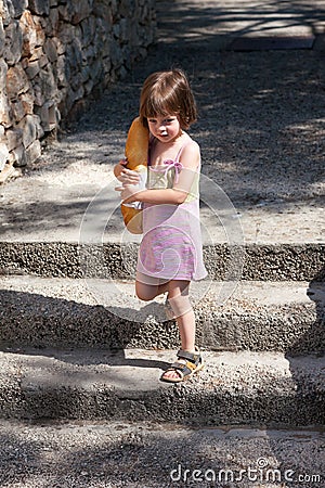 Adorable little girl walking and holding a loaf of bread Stock Photo