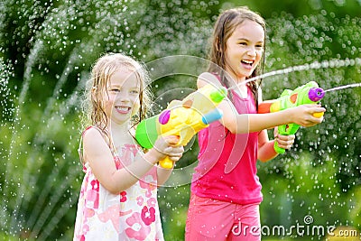 Adorable little girls playing with water guns on hot summer day. Cute children having fun with water outdoors. Stock Photo