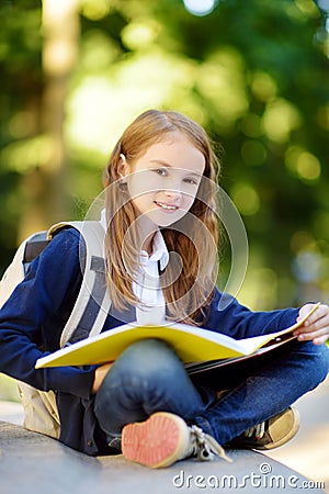 Adorable little schoolgirl studying outdoors on bright autumn day. Young student doing her homework. Education for small kids. Stock Photo