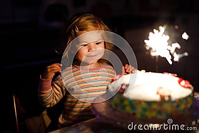 Adorable little toddler girl celebrating second birthday. Baby child eating marshmellows decoration on homemade cake Stock Photo