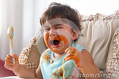 Adorable little toddler girl or infant baby crying when unsatisfied when finished eating food on baby chair. Cute infant girl get Stock Photo