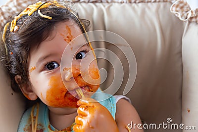 Adorable little toddler girl or infant baby eating delicious spaghetti food with tomato sauce. Funny cute infant girl get hungry Stock Photo