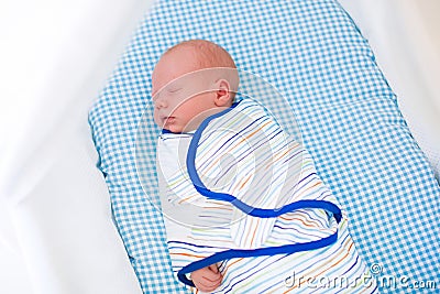 Adorable newborn baby sleeping swaddled in white bed. Stock Photo