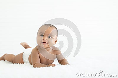 Adorable newborn Nigerian Asian baby girl wear diaper smiling with sparkling bright eyes and crawling on fluffy carpet on bed Stock Photo