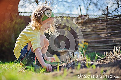 Adorable preschooler girl in yellow cardigan planting flowers in spring sunny garden Stock Photo