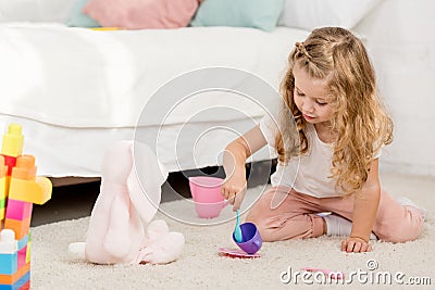 adorable preschooler playing with rabbit toy and plastic cups Stock Photo