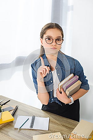 adorable preteen child showing one finger up and holding books Stock Photo