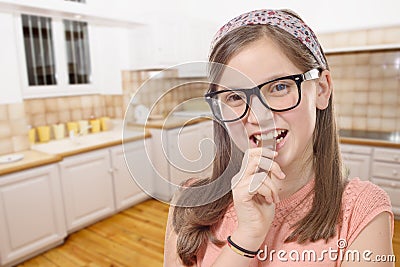 adorable preteen girl with glasses eats chocolate, kitchen background Stock Photo