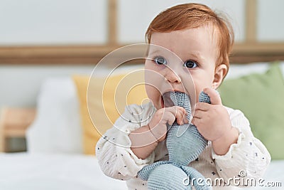Adorable redhead toddler sucking doll sitting on bed at bedroom Stock Photo