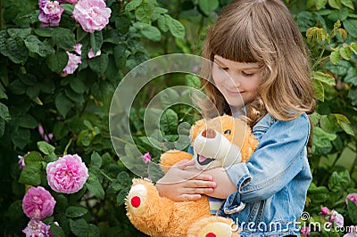 Adorable smiling girl with teddy bear in park with pink rose. Stock Photo