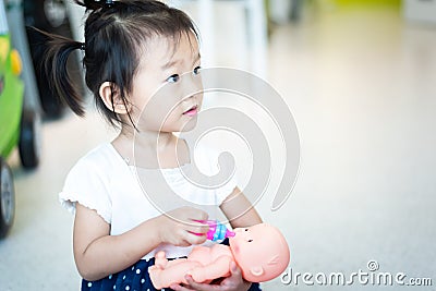 Sweet Asian little baby child playing doll, feeding bottle milk to baby doll Stock Photo