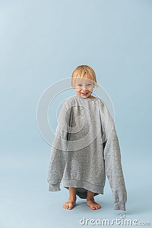 Adorable toddler boy in a huge oversized grey longsleeve over blue Stock Photo