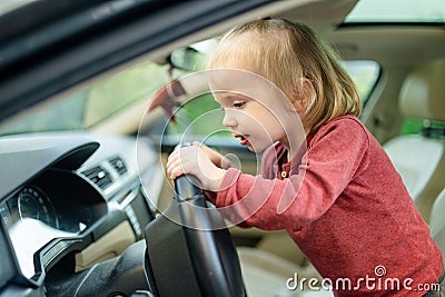 Adorable toddler boy playing in the driver`s seat. Cute little son sitting in fathers car Stock Photo