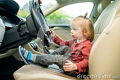 Adorable toddler boy playing in the driver`s seat. Cute little son sitting in fathers car Stock Photo