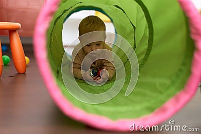 Adorable toddler crawling throw tunnel toy holding cars at kindergarten Stock Photo