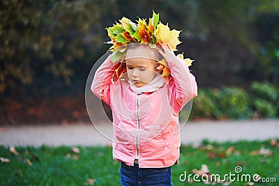 Adorable toddler girl in fallen leaves wreath in autumn park Stock Photo
