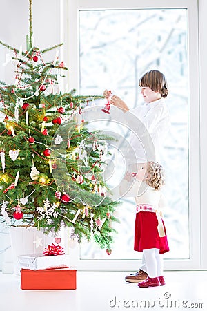 Adorable toddler girl helping her brother to decorate a beautiful Christmas tree Stock Photo