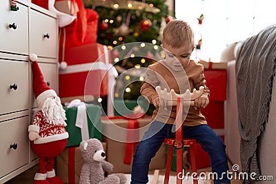 Adorable toddler playing on reindeer rocking by christmas tree at home Stock Photo