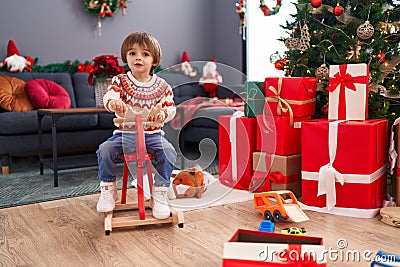 Adorable toddler playing on reindeer rocking by christmas tree at home Stock Photo