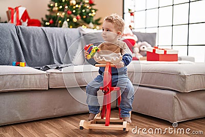 Adorable toddler playing on reindeer rocking by christmas tree at home Stock Photo