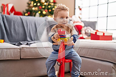 Adorable toddler playing on reindeer rocking by christmas tree at home Stock Photo