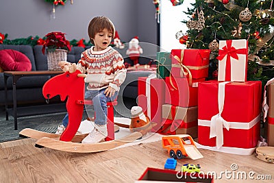 Adorable toddler playing on reindeer rocking by christmas tree at home Stock Photo
