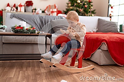 Adorable toddler playing on reindeer rocking by christmas tree at home Stock Photo