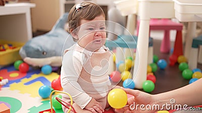 Adorable toddler sitting on floor looking ball crying at kindergarten Stock Photo