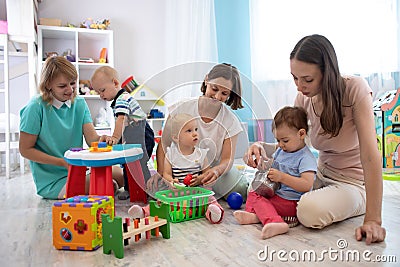 Adorable toddlers playing with colorful toys and mothers in nursery room. Nursery babies playing with adults in day care Stock Photo