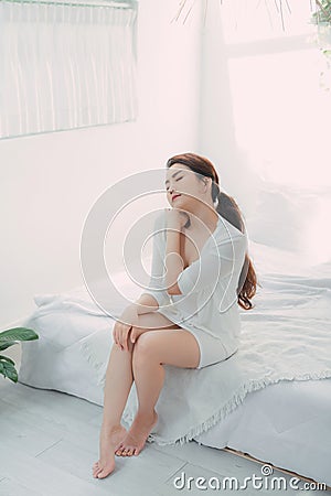 Adult attractive dreamy lady touching neck sitting bed Stock Photo