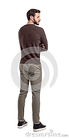 An adult bearded man in casual sweater stands in a back view half turned to look behind his shoulder. Stock Photo