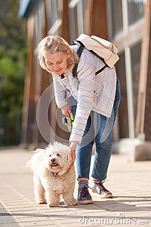 Adult blond woman walking with fluffy white dog in summer city Stock Photo