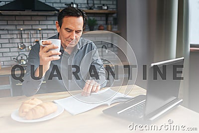 Adult businessman sit at table in kitchen anr read journal. He hold white cup and look down. Laptop and plate with Stock Photo