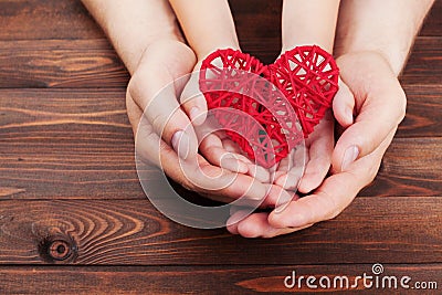 Adult and child holding red heart in hands over a wooden table. Family relationships, health care, pediatric cardiology concept. Stock Photo