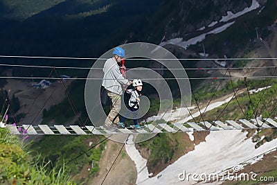 Adult and child on a rope bridge in the mountains Stock Photo