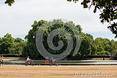 Adult couple cycling next to a pond in Hyde Park, London, UK Editorial Stock Photo