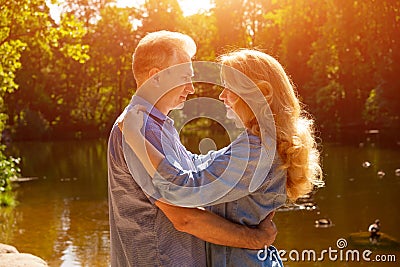 An adult couple stand on the shore of the lake in an embrace in the rays of the setting sun Stock Photo