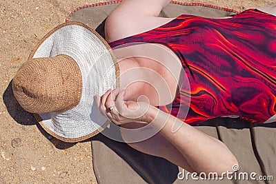 An adult elderly woman in a swimsuit lies on the sandy shore, covering her face with a hat. Travel and tourism retired Stock Photo